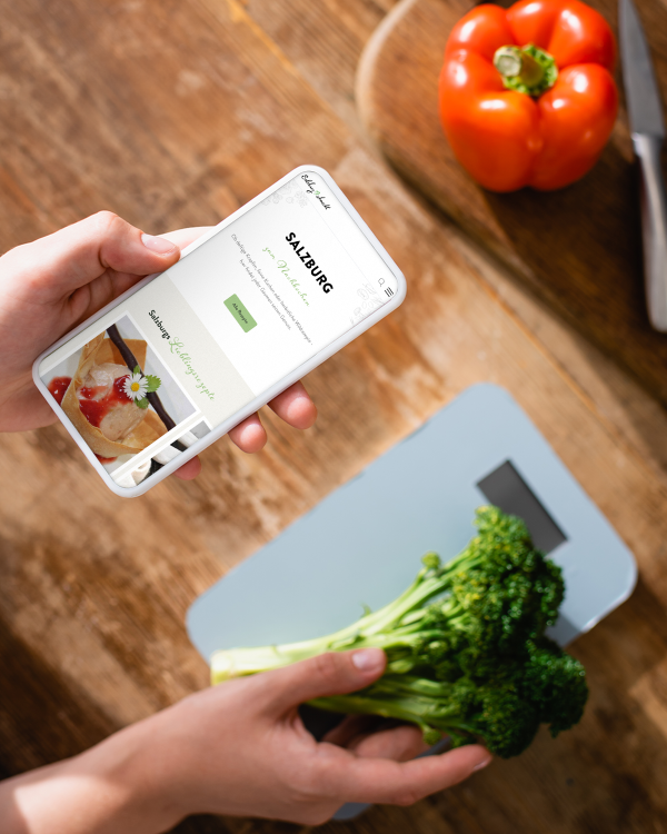 Frau hält Handy in der Hand während sie in der Küche kocht